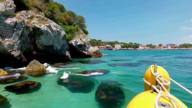 Gorgeous 4K coastal video of a wild sun drenched Mediterranean shoreline highlighting crystal clear turquoise waters lapping against rugged stone cliffs while bright yellow safety buoys bob gently on