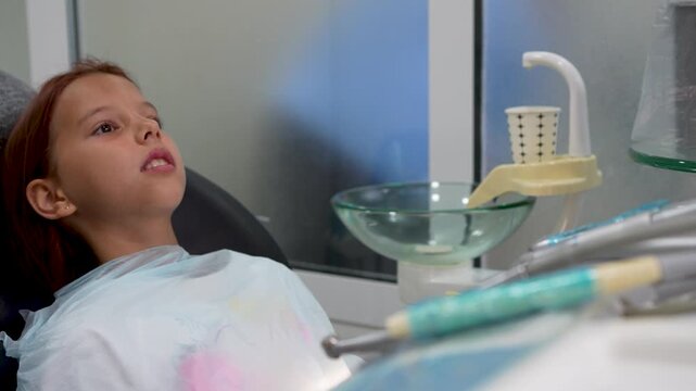 Little girl sitting in dental chair during treatment pause in clinic close up.