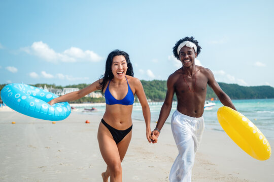 Friends, diverse couple having fun with colorful inflatable rings at the seaside