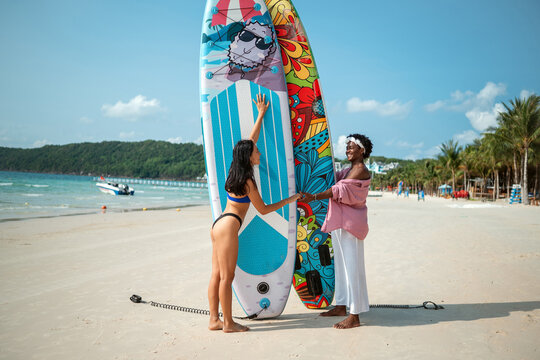 Young multiethnic people, couple having fun on surfboards in the clear ocean water during summer