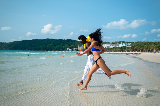 Happy couple running on a sandy beach with inflatable rings during a tropical vacation