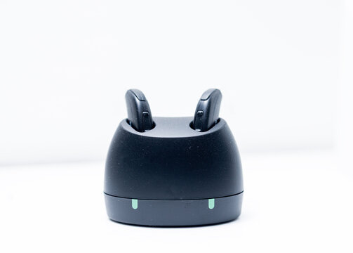 Pair of modern rechargeable hearing aids in charging station isolated on a white background with copy space