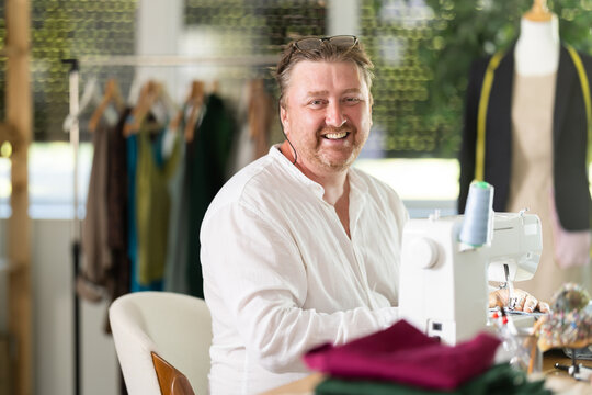 Happy middle-aged male dressmaker working with sewing-machine