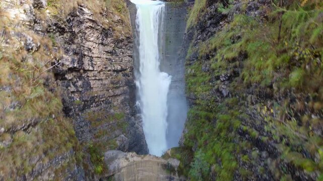 Drone view of a majestic waterfall flowing into the turquoise river inside Vajont canyon, Italy. Scenic aerial shot of steep rock cliffs and rushing water