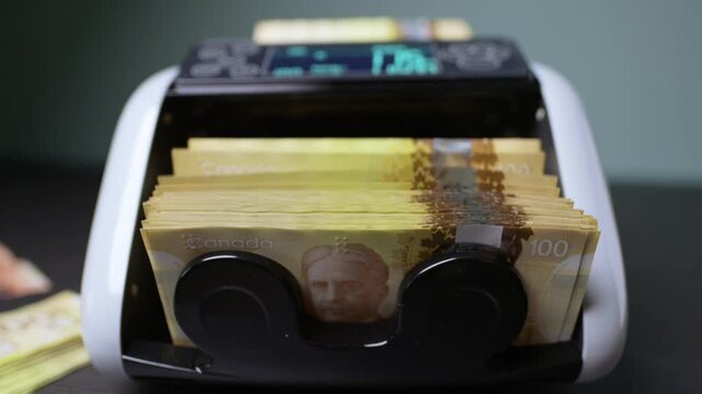 Counting Canadian dollars with an automatic machine in a slow motion spectacle of finance and investment