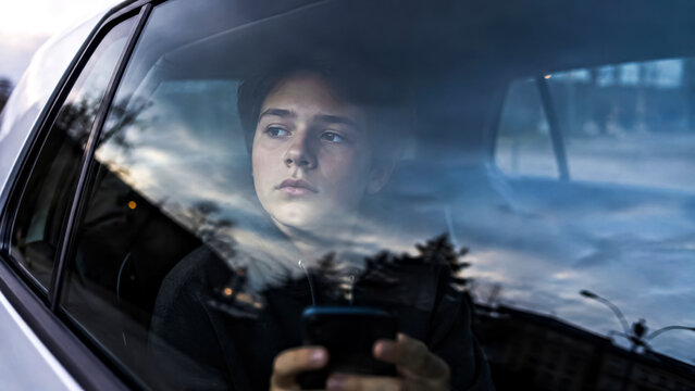 Teenager Seen Through the Reflective Window from Outside the Car, Holding Smartphone in Hands