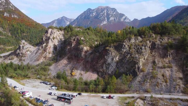 Aerial 4K drone view of Vajont valley in autumn with the lake. Scenic Italian Dolomites landscape with turquoise water, winding mountain road, and vibrant fall foliage forest in October.