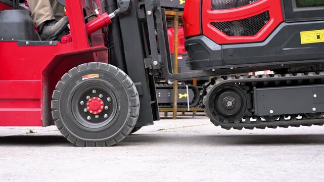 Close-up shot of a red forklift lifting a mini excavator during a warehouse logistics operation. High quality 4k footage