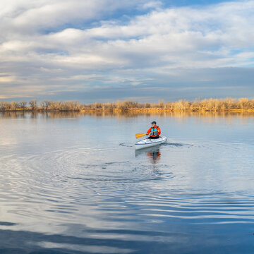 lonely paddler in an expedition canoe on calm lake in Colorado in early spring scenery