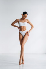 Fototapeta na wymiar Slim female model in white bikini poses gracefully against a minimalist background, showcasing an ideal body shape and emphasizing fitness and health aesthetics