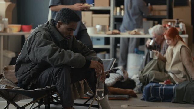 Young adult African American man receiving plate of food from Middle Eastern volunteer in shelter and starting friendly conversation. Clip suitable for humanitarian aid campaigns and nonprofit promos