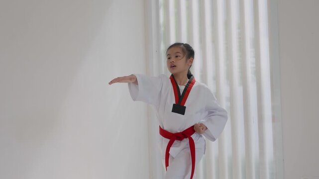 Child practices karate moves in a training room while wearing a white uniform and red belt
