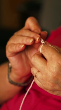 Woman's hands crocheting white yarn in warm light at home.