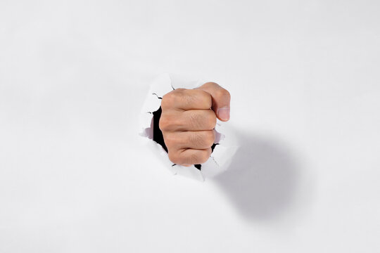 Male fist punching through a torn white paper hole, power and determination concept.