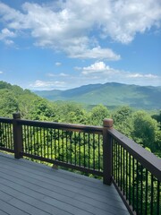 Fototapeta premium Scenic wooden balcony overlooking lush green valley with distant mountains under cloudy sky