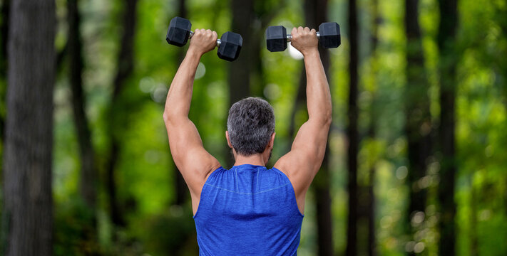 Strong man do sport exercise. Outdoor workout. Sport athlete man with dumbbell. Healthy lifestyle. Biceps muscle. Strong triceps. Man exercising with dumbbell. Man athlete lifting dumbbell, back view