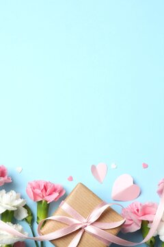 Beautiful carnations with gift box on pastel blue background. Top vertical view