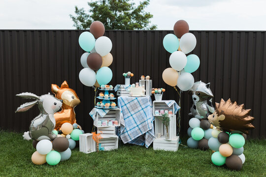Festive birthday sweet table candy bar decoration with forest animals theme and balloons outdoors.