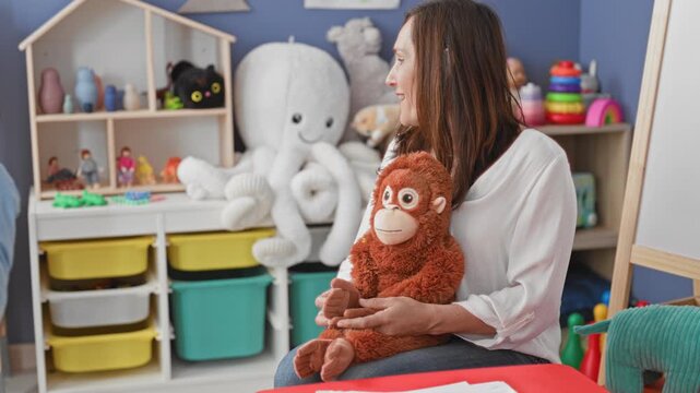 Woman holding plush monkey and speaking to little boy in a child playroom building; nurturing play learning.