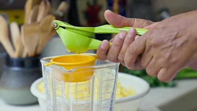 Hands squeezing fresh lime juice using a green manual press into a blender