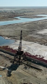 Vertical footage of the abandoned Aral Sea port with rusted cranes and railway, a haunting reminder of the vanished sea and fishing industry.