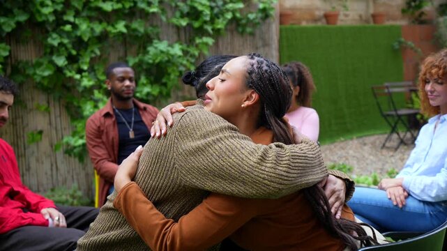 Diverse group of people sitting in a circle during an outdoor therapy session, showing support and empathy as two members share an emotional hug, promoting mental health and healing together