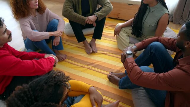 Group of diverse individuals sitting in a circle on the floor, engaging in a heartfelt conversation during a support meeting, sharing experiences and providing mutual emotional assistance
