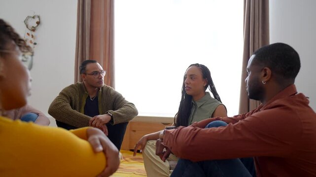 Diverse group of people sitting on the floor in a circle during a support meeting, listening intently as one woman shares her story and feelings with the compassionate and empathetic participants