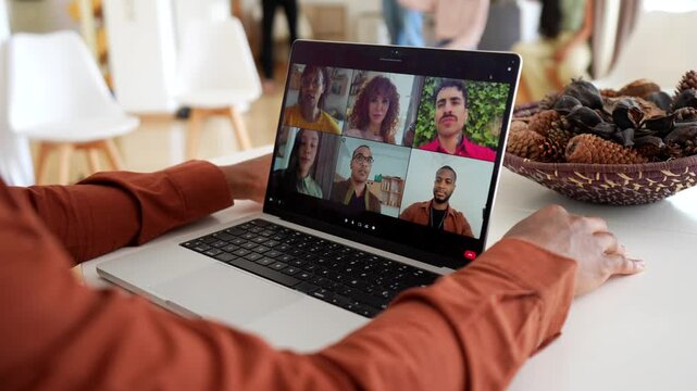 Over the shoulder view of a male psychologist leading a remote group therapy session via video conference on a laptop, with diverse people talking and listening from their homes