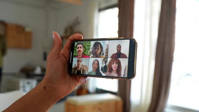 Female hand holding a smartphone during an online group therapy session with diverse participants, discussing and sharing experiences together through a video conference on a mobile device at home