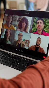 Over the shoulder view of a person using a laptop for a video conference with a diverse group of people engaged in an online meeting, discussing and sharing experiences during therapy