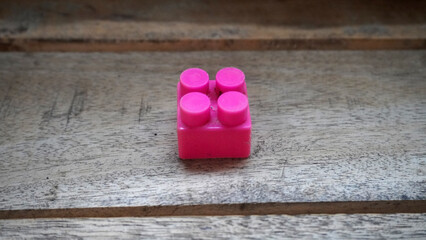 Single pink plastic building block resting on a wooden textured surface. © anungcamui