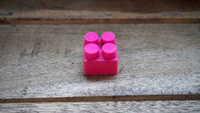 Single pink plastic building block resting on a wooden textured surface.
