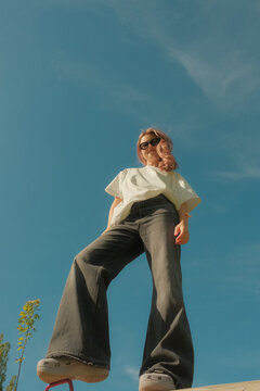 Beautiful carefree young woman with wavy hair in white t-shirt standing on blue sky background low angle shot.