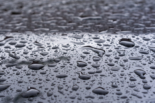 Close-up of a smooth metallic surface covered with water droplets of various sizes. 