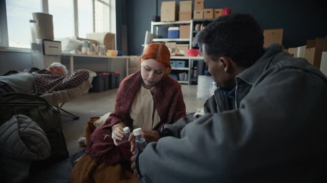 Young adult Caucasian woman and young adult Black man receiving bottled water from volunteer in temporary shelter. Clip suitable for humanitarian aid and non-profit organization promotions