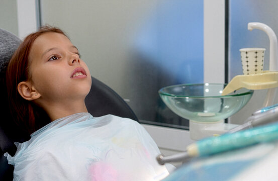Little girl sitting in dental chair during treatment pause in clinic close up.