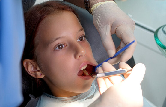 Close up high angle shot of a dentist in medical gloves using a metal carpule syringe and mirror to give an anesthetic injection into a young girl patient's mouth before a treatment procedure.