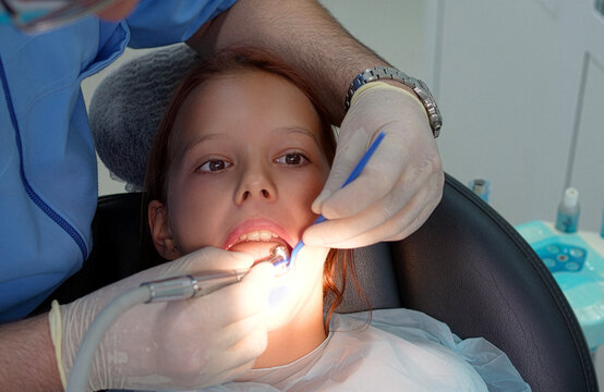 Dentist drilling little girl tooth with high speed handpiece under lamp close up