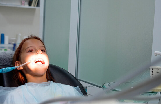 Little girl sitting in dental chair during treatment pause in clinic close up.