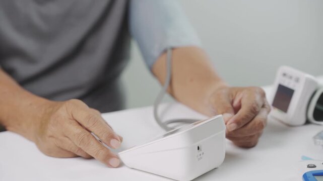Close up of a senior pressing the start button on a digital blood pressure monitor for home blood pressure measurement, representing hypertension monitoring, preventive healthcare, selfcare.