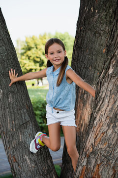 Joyful laughter fills the air as a little girl climbs a tree in a sunny park filled with nature