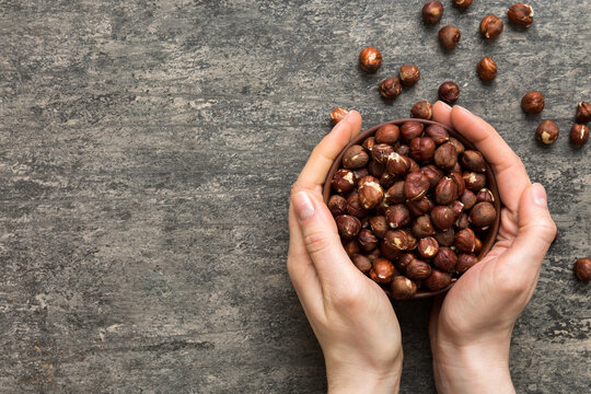 Woman hands holding a wooden bowl with hazelnut nuts. Healthy food and snack. Vegetarian snacks of different nuts
