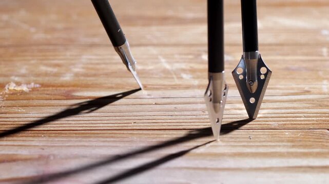 Professional archery arrows landing and standing upright on a textured wooden board, highlighting the sharp metal tips and clean design with high-contrast cinematic lighting.