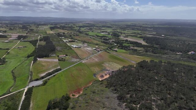 A drone pushes in and booms up over lush green fields, scattered houses, and dense forests in the beautiful Portuguese countryside, part of the Fisherman's Trail.