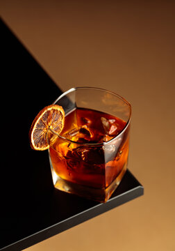 Old-fashioned cocktail with ice and a dried orange slice on a black table.