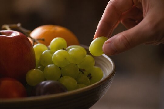 A single green grape being taken from a full fruit bowl, soft light.