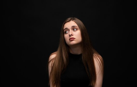Young woman showing annoyance, boredom, and indifference with a sidelong glance on black background