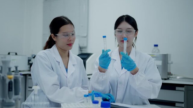 Two female asian scientists working in a research laboratory discussing a scientific experiment and holding test tubes