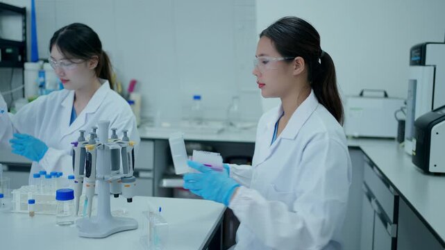 Two female scientists collaborating on medical research and experimenting with a multichannel pipette in a modern laboratory